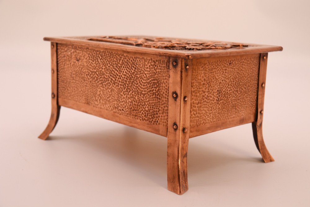 A rectangular Arts and Crafts copper box featuring a hand-hammered texture, splayed legs, and an embossed lid with a floral design and the word TABAC. View XIX
