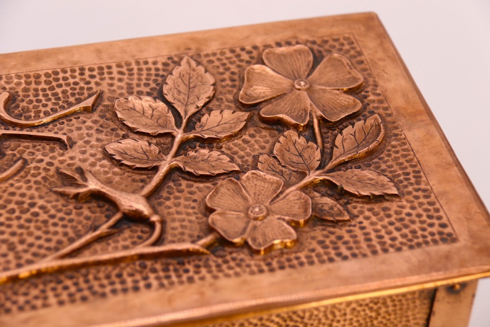 A rectangular Arts and Crafts copper box featuring a hand-hammered texture, splayed legs, and an embossed lid with a floral design and the word TABAC. View XXI