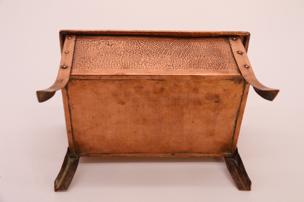 A rectangular Arts and Crafts copper box featuring a hand-hammered texture, splayed legs, and an embossed lid with a floral design and the word TABAC. View XXII