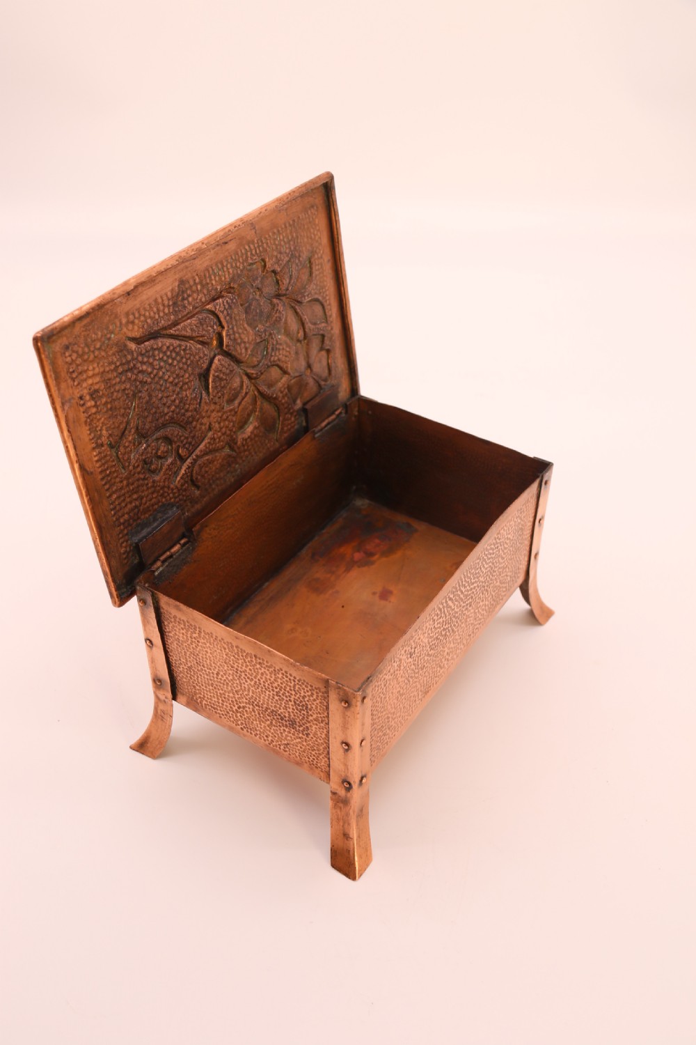 A rectangular Arts and Crafts copper box featuring a hand-hammered texture, splayed legs, and an embossed lid with a floral design and the word TABAC. View XXIII