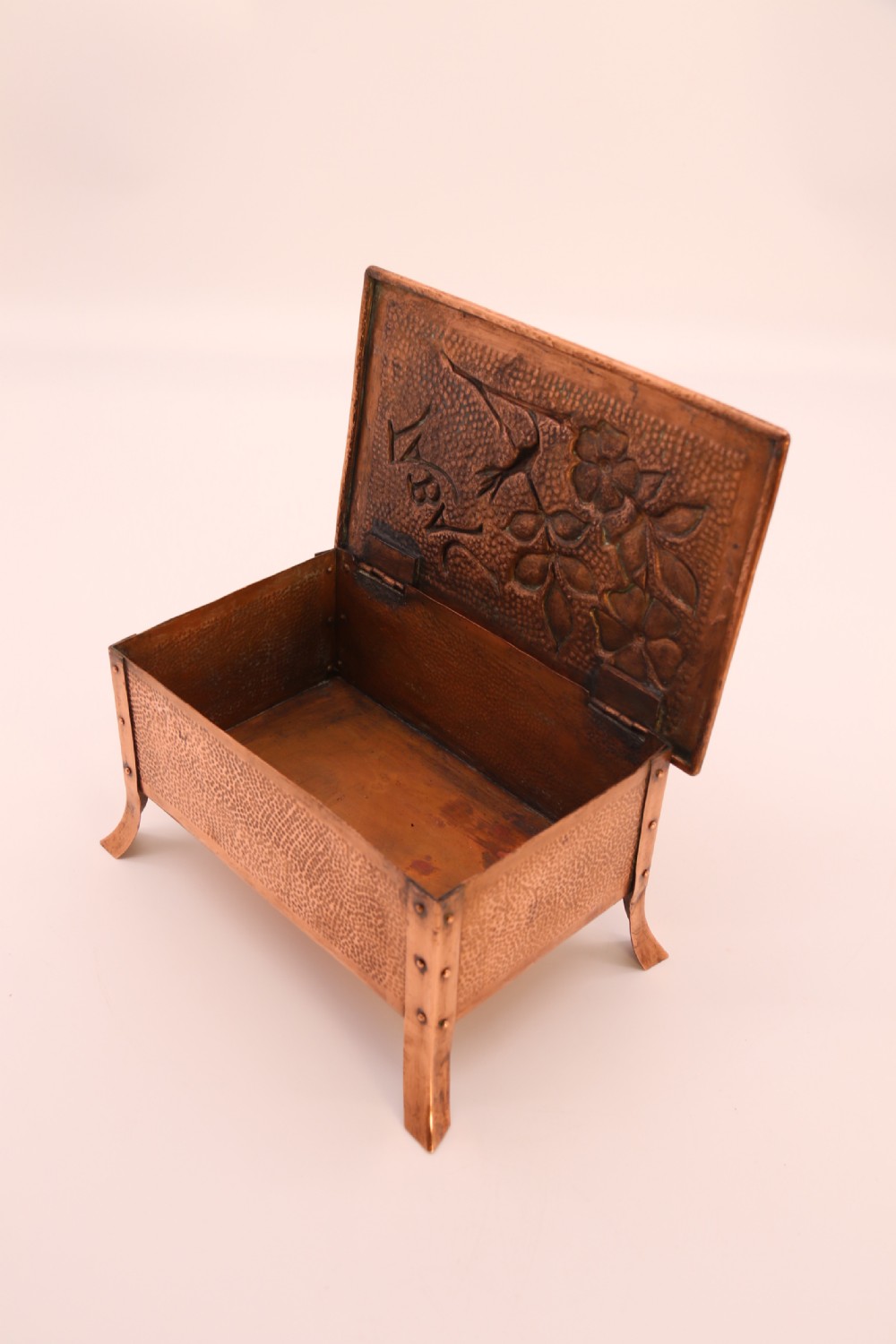 A rectangular Arts and Crafts copper box featuring a hand-hammered texture, splayed legs, and an embossed lid with a floral design and the word TABAC. View XXVII