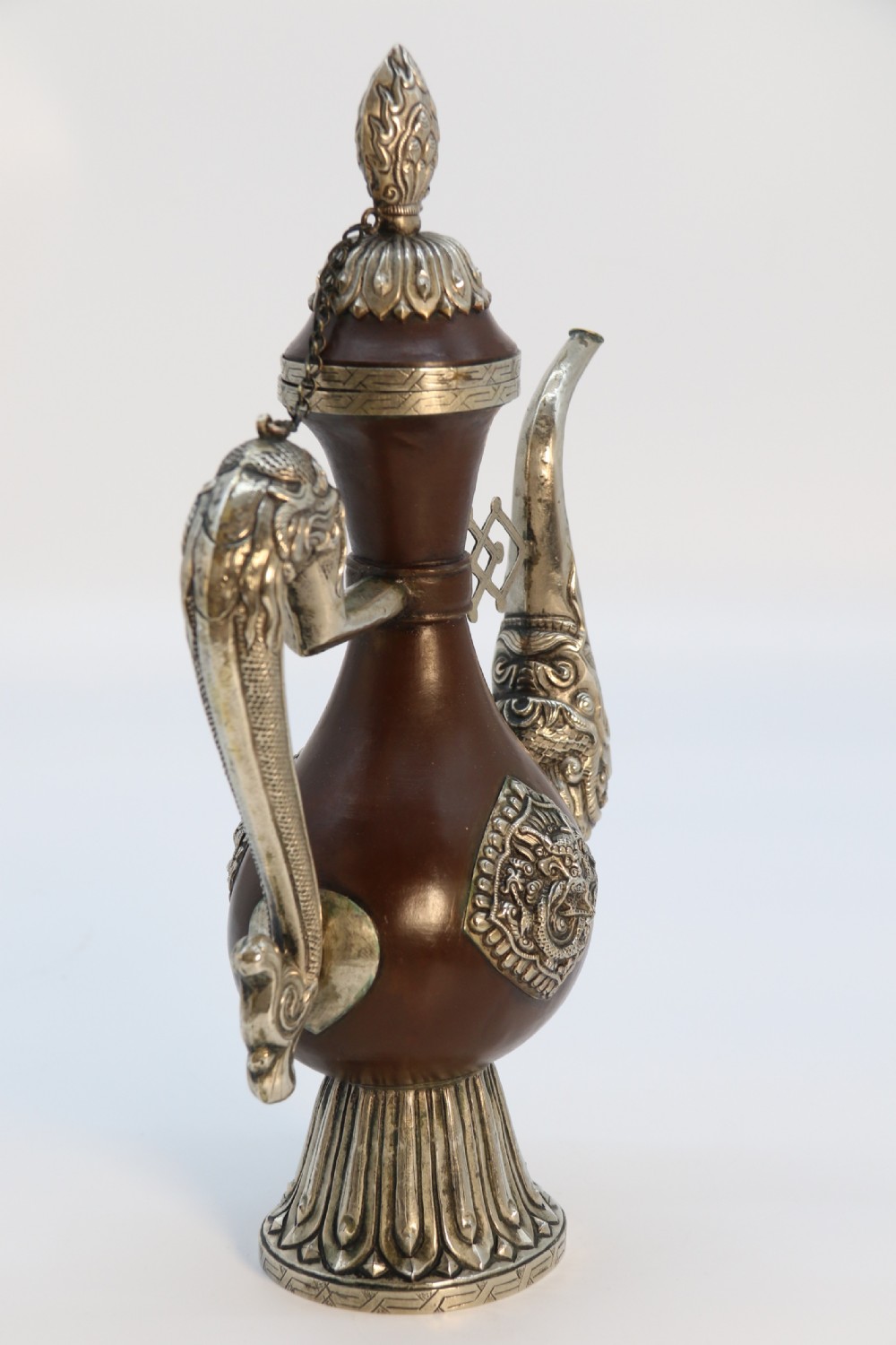 An antique Indo-Tibetan ritual ewer featuring a dark brown bulbous body, repousse silver dragon spout and handle, lotus base, and chained lid finial. View III