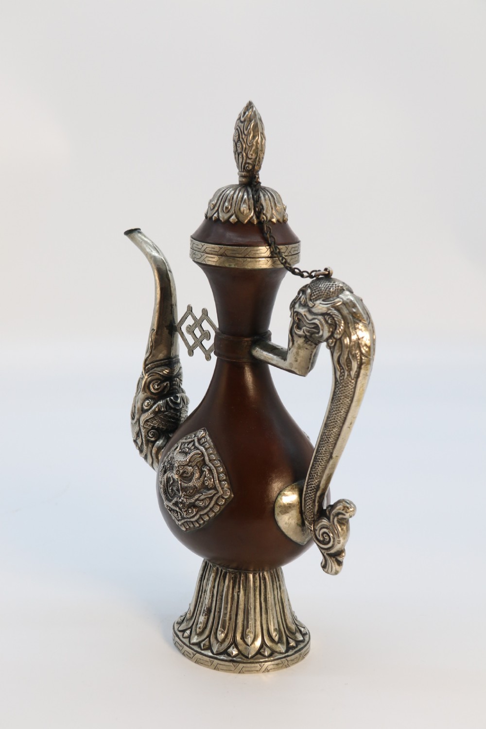 An antique Indo-Tibetan ritual ewer featuring a dark brown bulbous body, repousse silver dragon spout and handle, lotus base, and chained lid finial. View VI