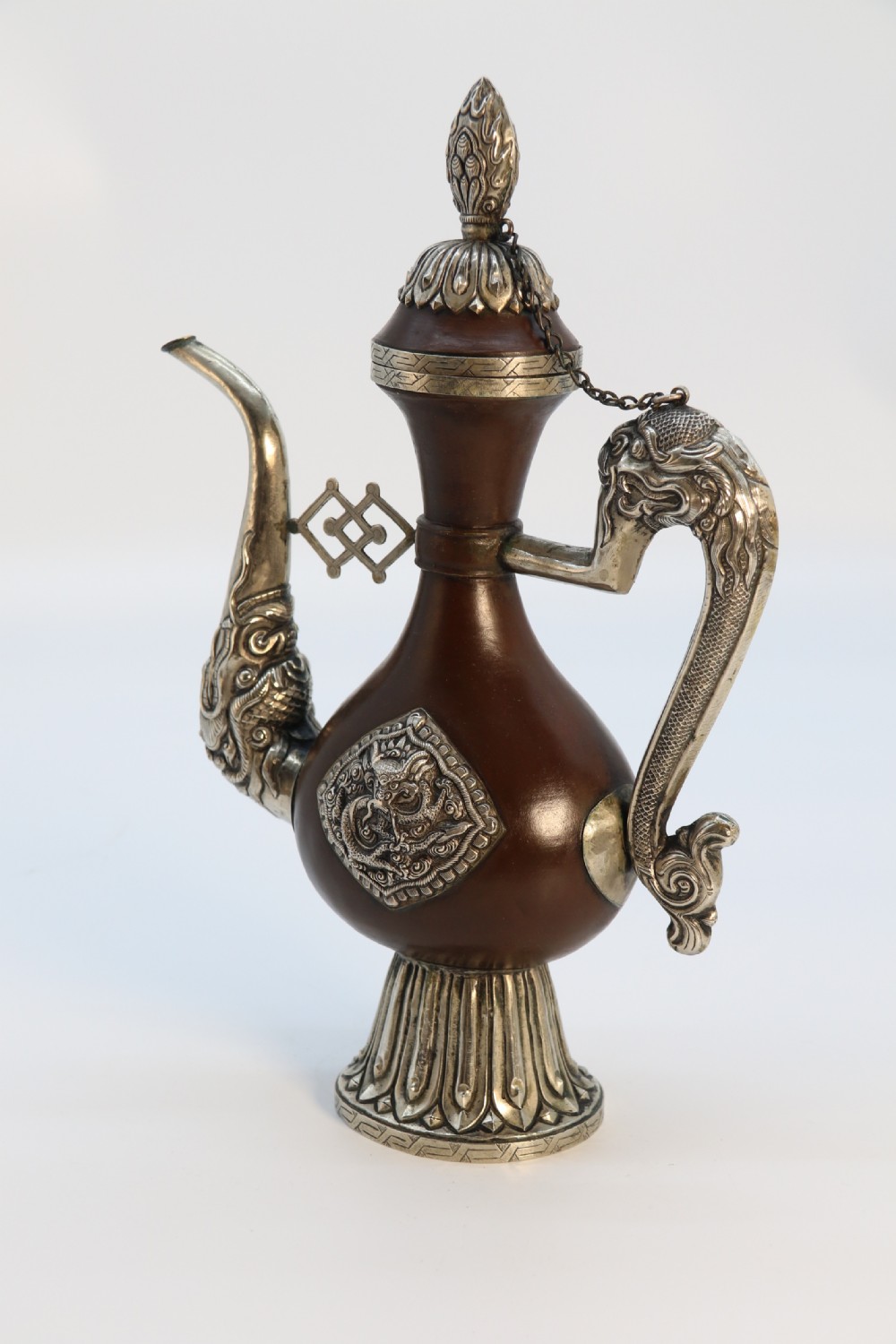 An antique Indo-Tibetan ritual ewer featuring a dark brown bulbous body, repousse silver dragon spout and handle, lotus base, and chained lid finial. View VII