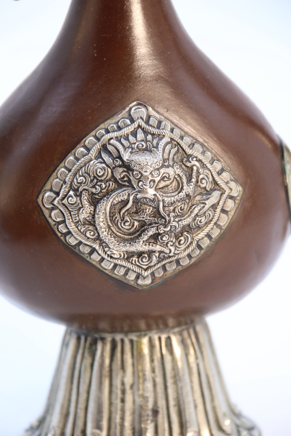An antique Indo-Tibetan ritual ewer featuring a dark brown bulbous body, repousse silver dragon spout and handle, lotus base, and chained lid finial. View VIII