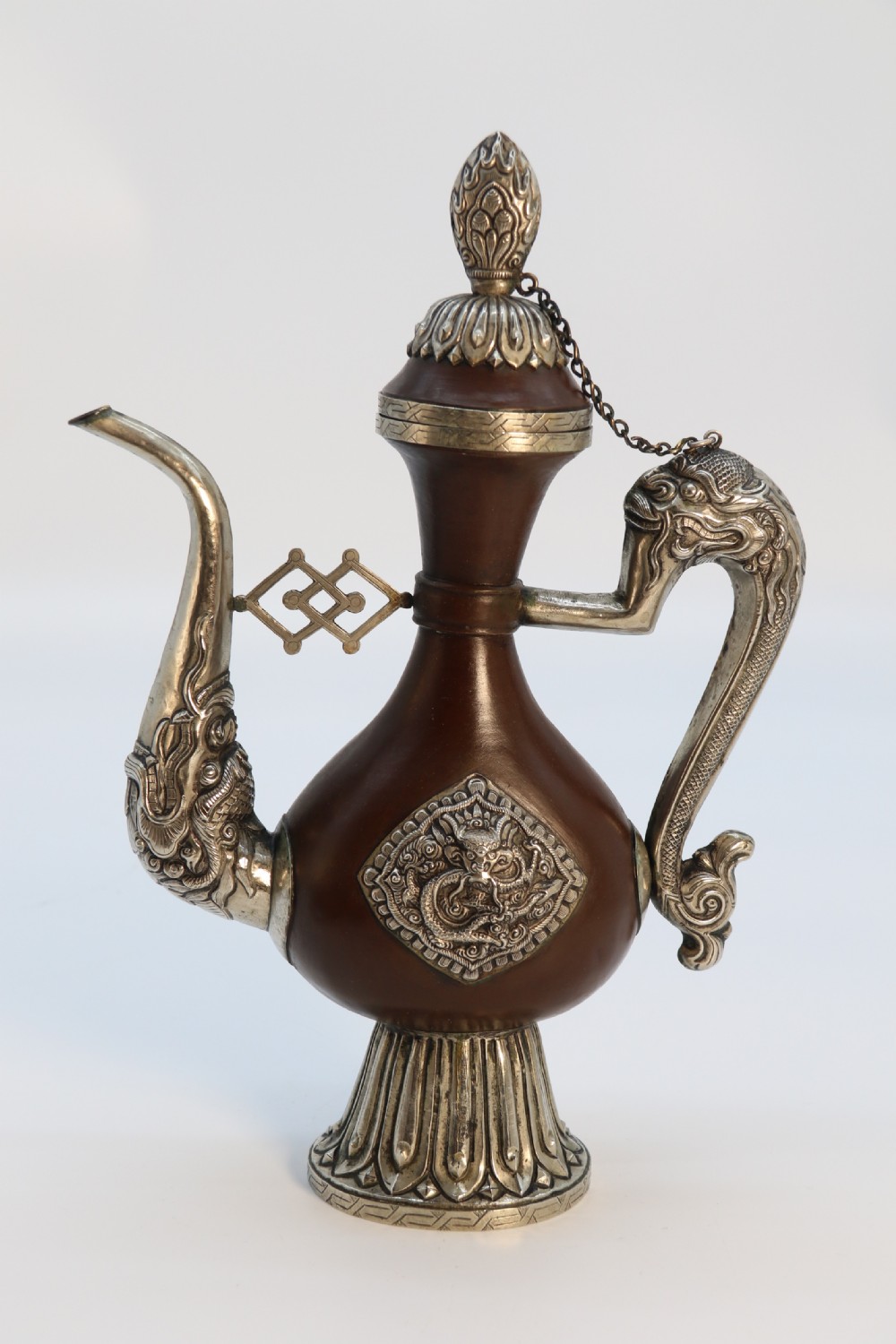 An antique Indo-Tibetan ritual ewer featuring a dark brown bulbous body, repousse silver dragon spout and handle, lotus base, and chained lid finial. View IX