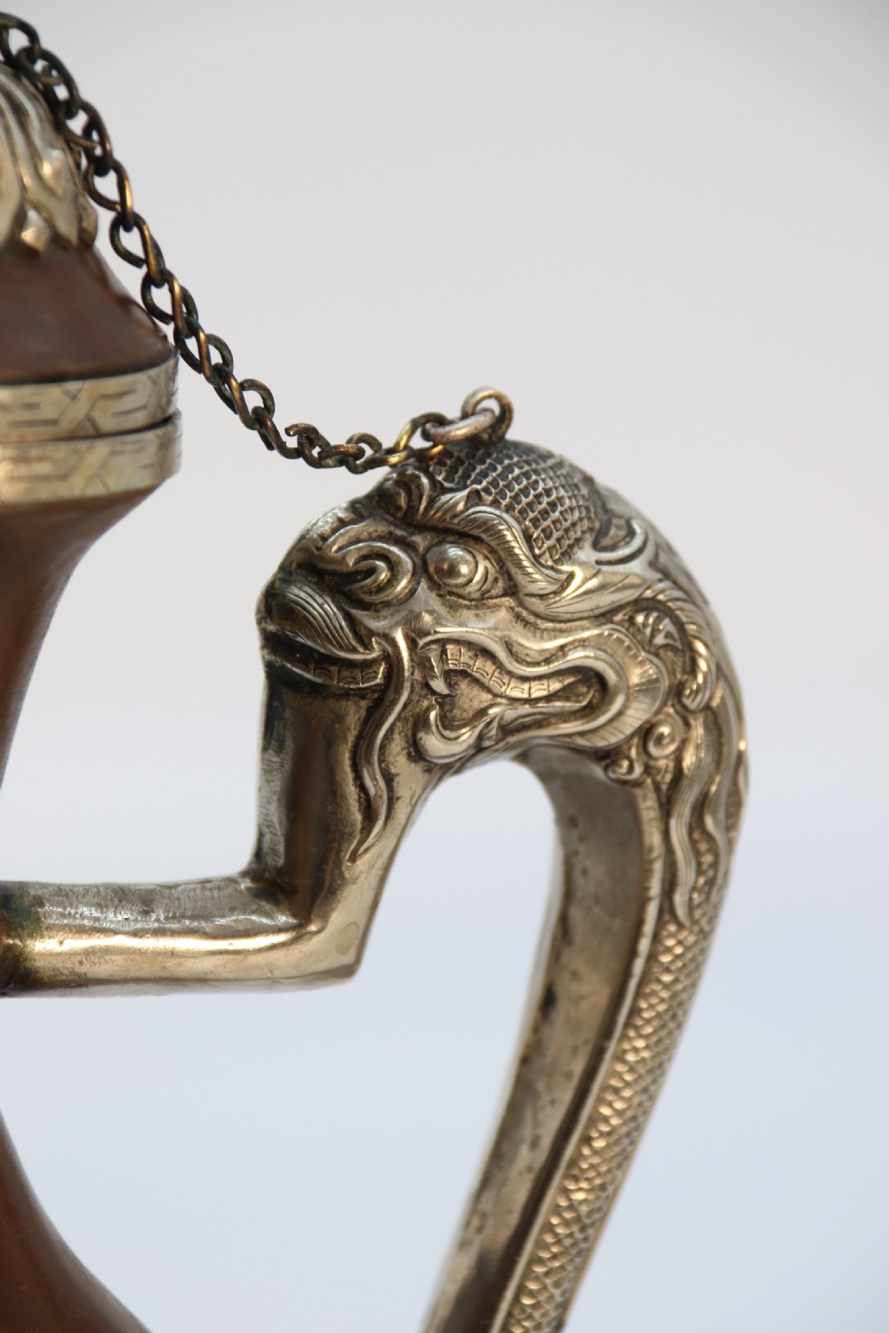 An antique Indo-Tibetan ritual ewer featuring a dark brown bulbous body, repousse silver dragon spout and handle, lotus base, and chained lid finial. View X