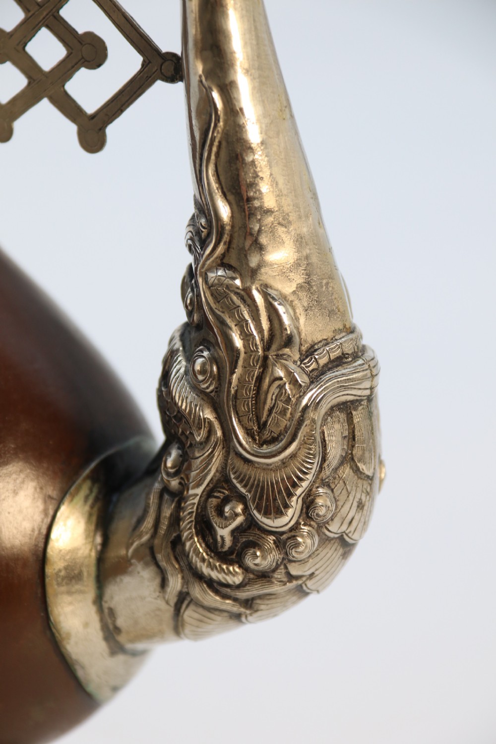 An antique Indo-Tibetan ritual ewer featuring a dark brown bulbous body, repousse silver dragon spout and handle, lotus base, and chained lid finial. View XII