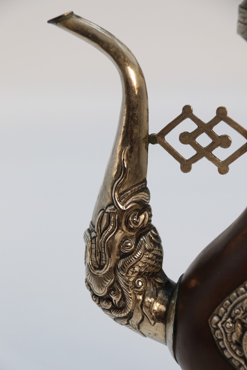 An antique Indo-Tibetan ritual ewer featuring a dark brown bulbous body, repousse silver dragon spout and handle, lotus base, and chained lid finial. View XV
