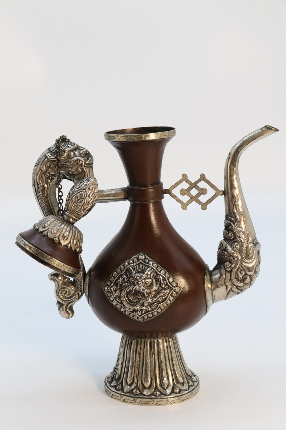 An antique Indo-Tibetan ritual ewer featuring a dark brown bulbous body, repousse silver dragon spout and handle, lotus base, and chained lid finial. View XIX