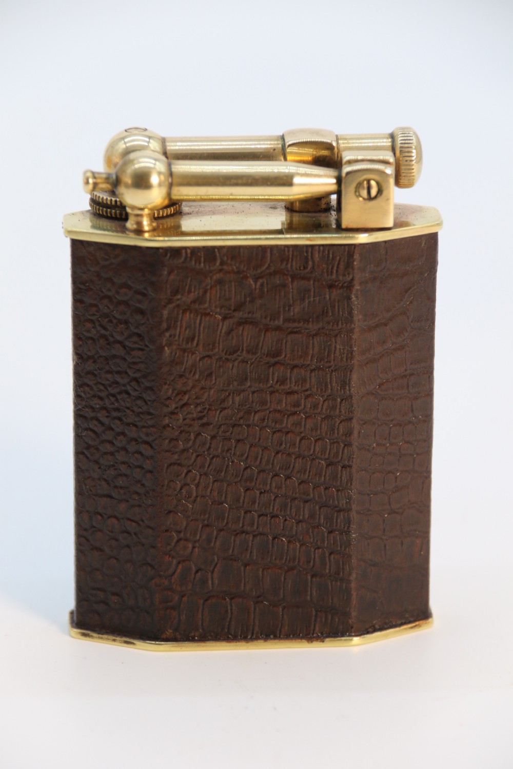 An Art Deco table lighter featuring a brown crocodile-embossed leather body with a solid brass base and upper lift-arm mechanism.