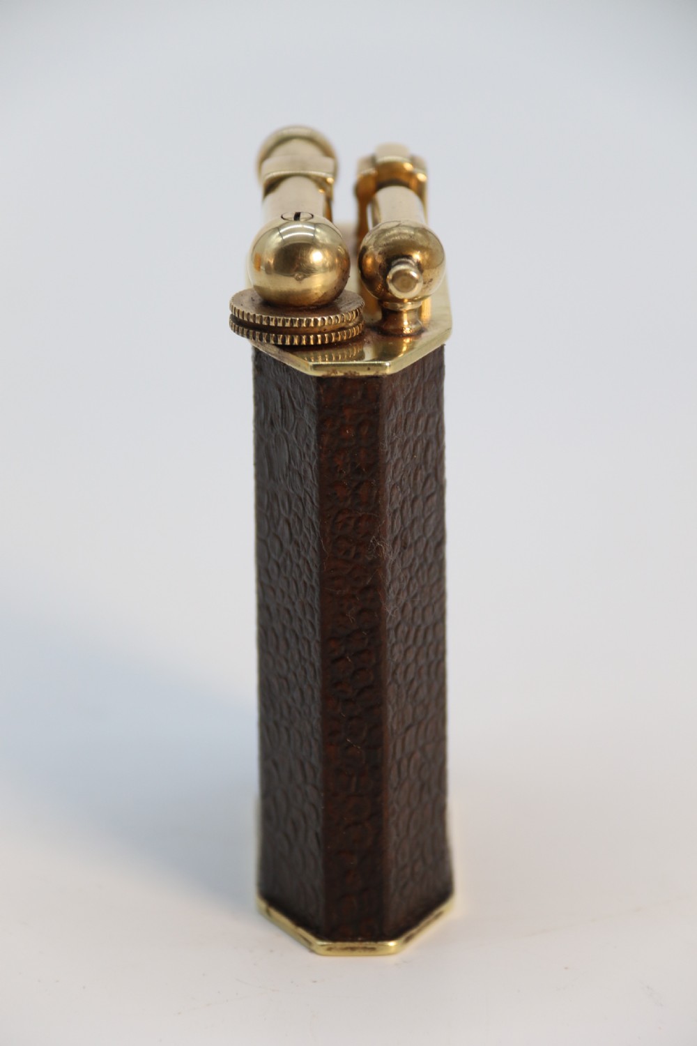 An Art Deco table lighter featuring a brown crocodile-embossed leather body with a solid brass base and upper lift-arm mechanism. View V