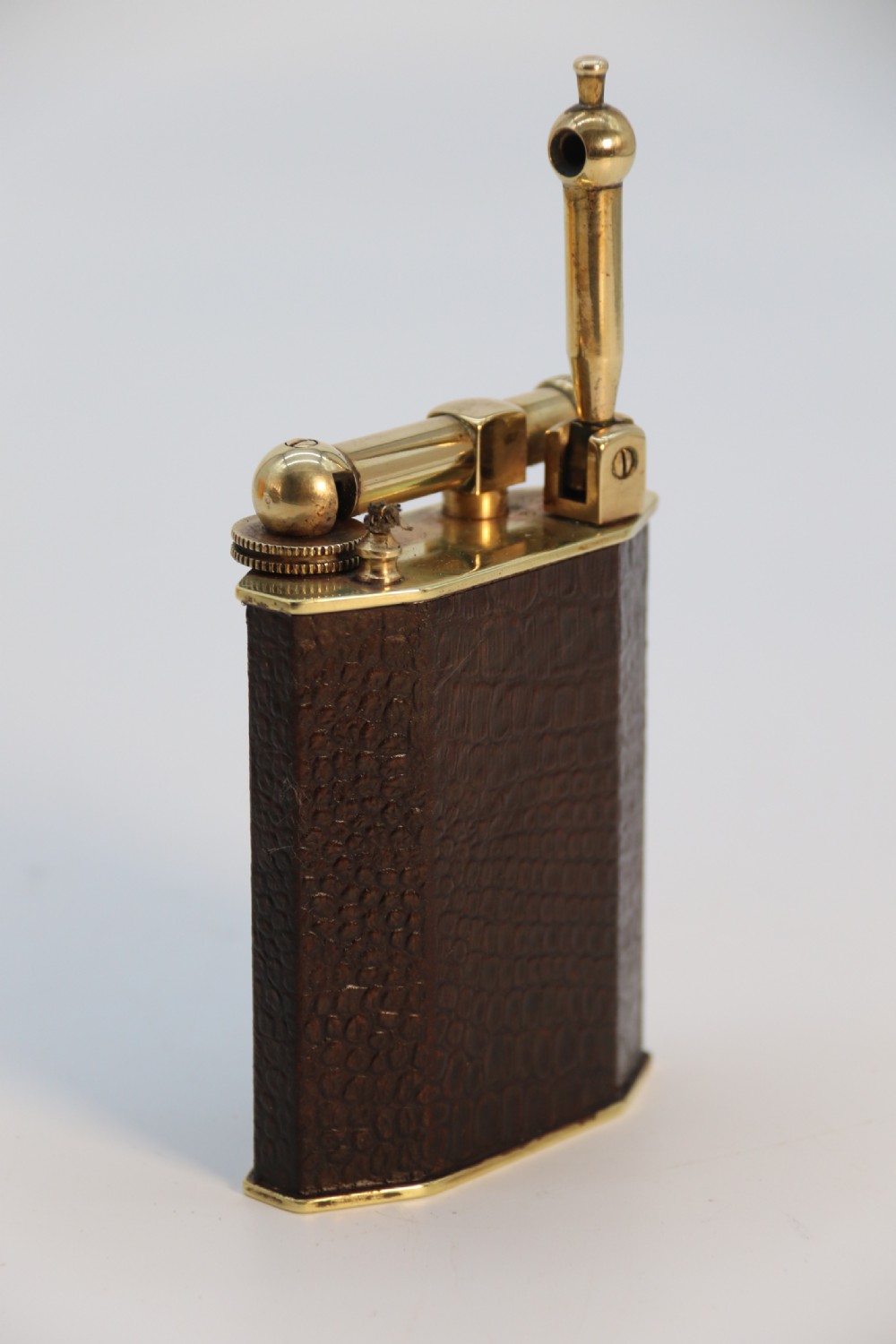 An Art Deco table lighter featuring a brown crocodile-embossed leather body with a solid brass base and upper lift-arm mechanism. View VIII