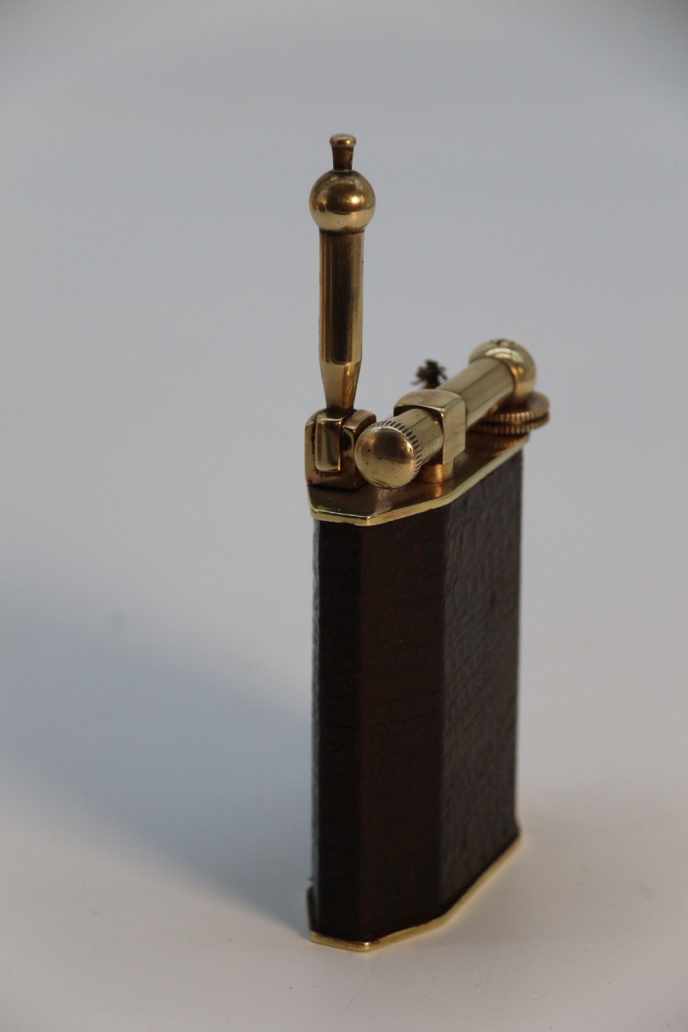 An Art Deco table lighter featuring a brown crocodile-embossed leather body with a solid brass base and upper lift-arm mechanism. View IX