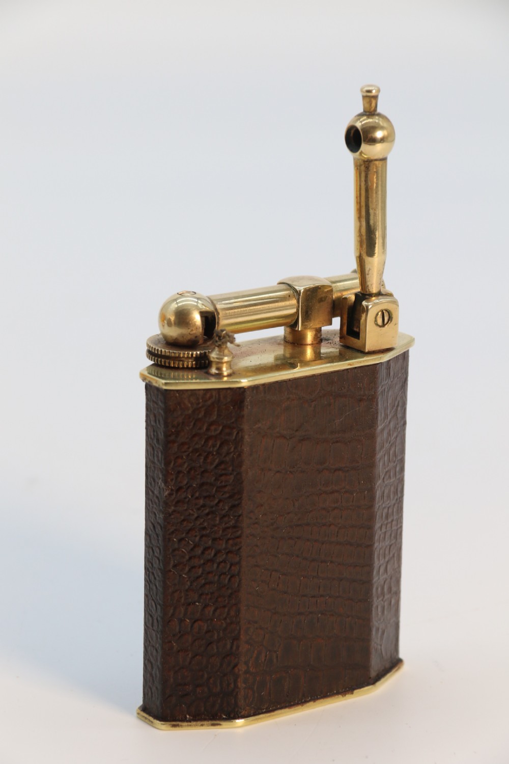 An Art Deco table lighter featuring a brown crocodile-embossed leather body with a solid brass base and upper lift-arm mechanism. View XI