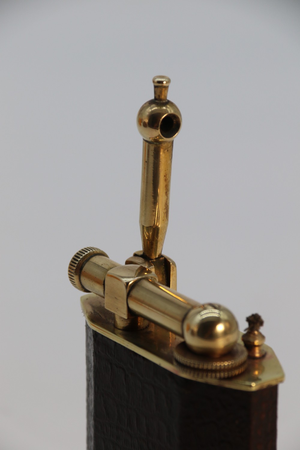 An Art Deco table lighter featuring a brown crocodile-embossed leather body with a solid brass base and upper lift-arm mechanism. View XVI