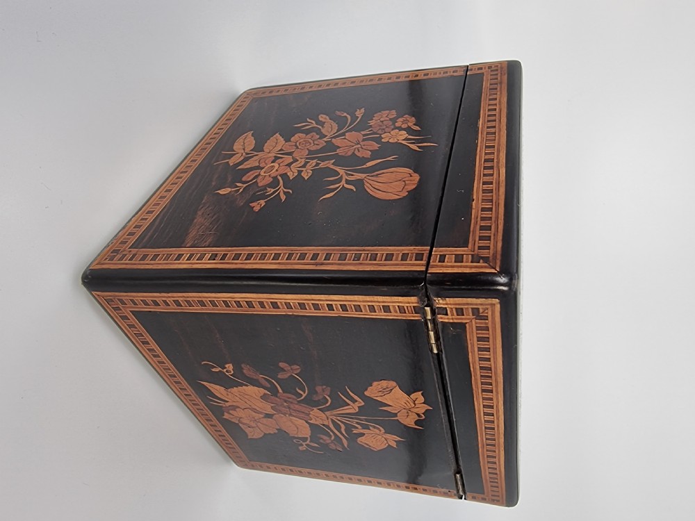 A square ebonised wooden box with Sorrento marquetry inlay depicting figures on the lid, floral sprays on the sides, and a key inserted in the keyhole. View VIII