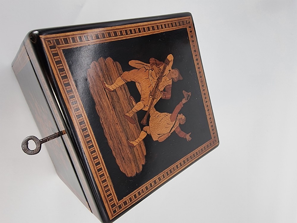 A square ebonised wooden box with Sorrento marquetry inlay depicting figures on the lid, floral sprays on the sides, and a key inserted in the keyhole. View XIX