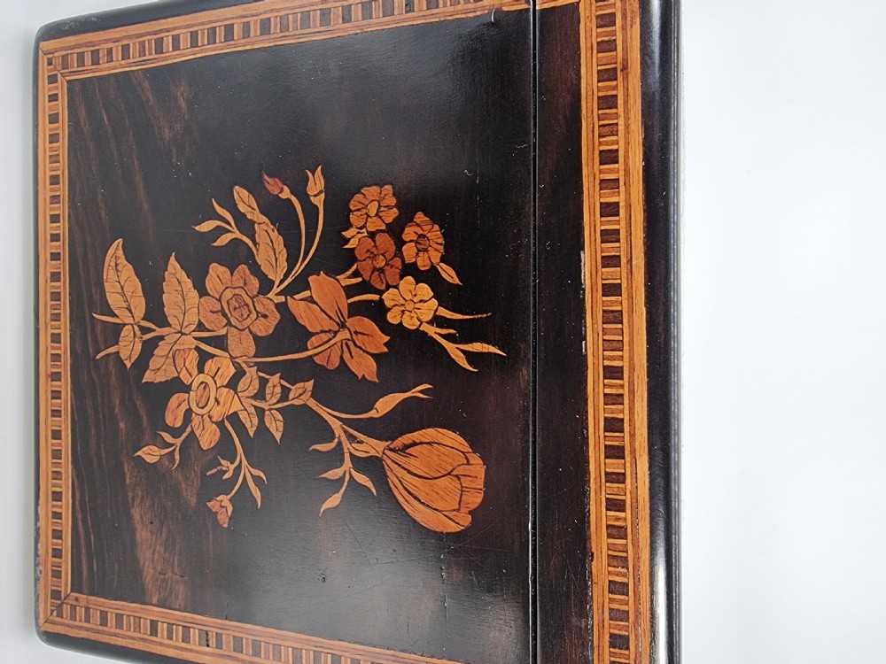 A square ebonised wooden box with Sorrento marquetry inlay depicting figures on the lid, floral sprays on the sides, and a key inserted in the keyhole. View XXIII
