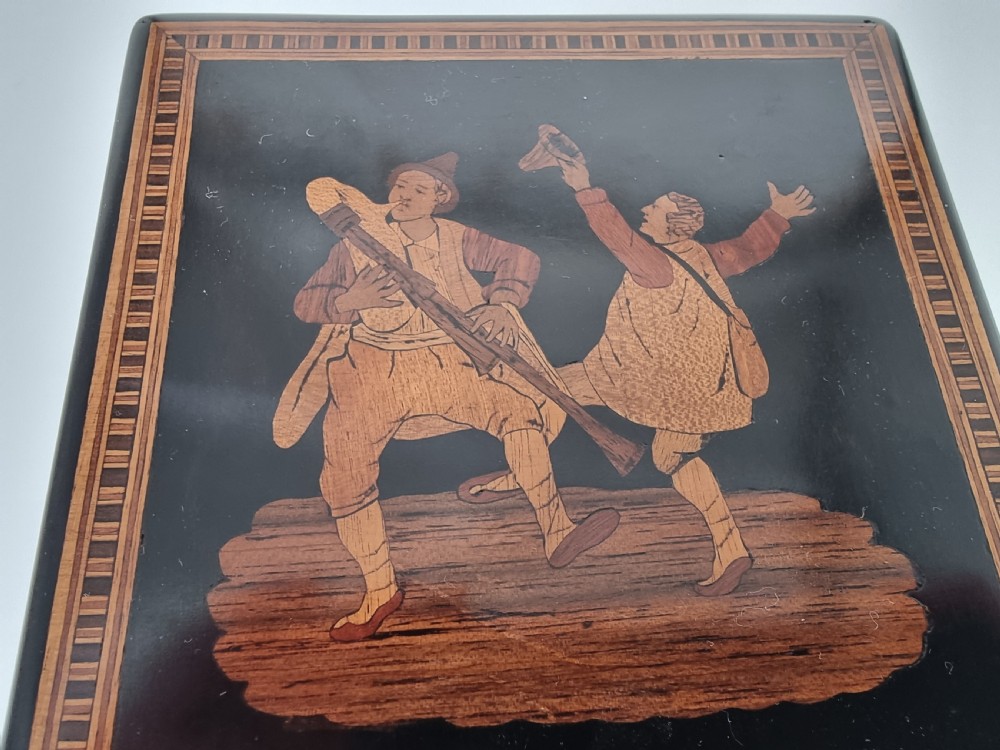 A square ebonised wooden box with Sorrento marquetry inlay depicting figures on the lid, floral sprays on the sides, and a key inserted in the keyhole. View XXIV