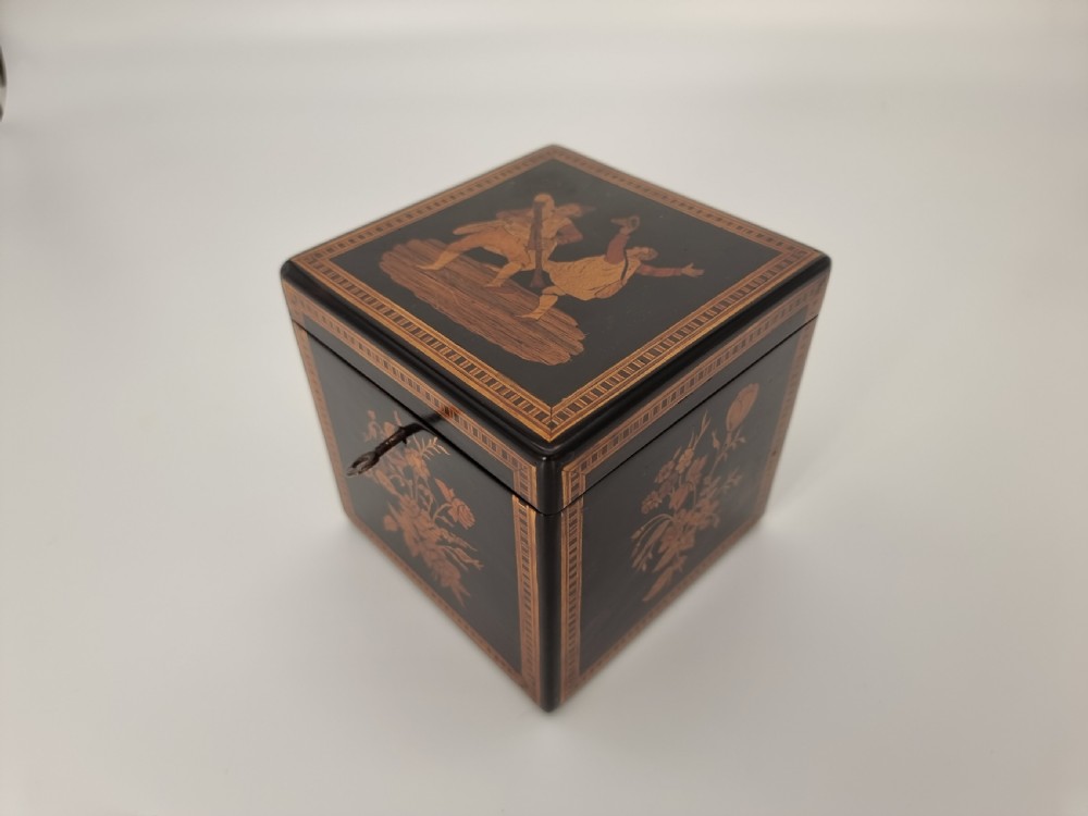 A square ebonised wooden box with Sorrento marquetry inlay depicting figures on the lid, floral sprays on the sides, and a key inserted in the keyhole. View XXVI