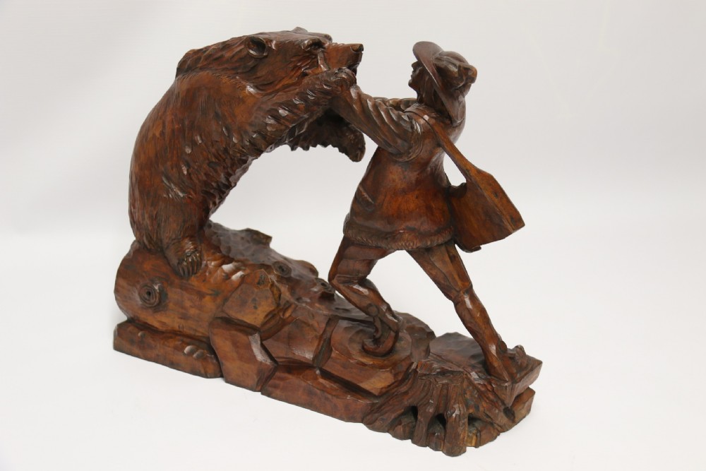 A late 19th-century carved wooden figure group depicting a huntsman battling a rearing bear on a log-form base. View II