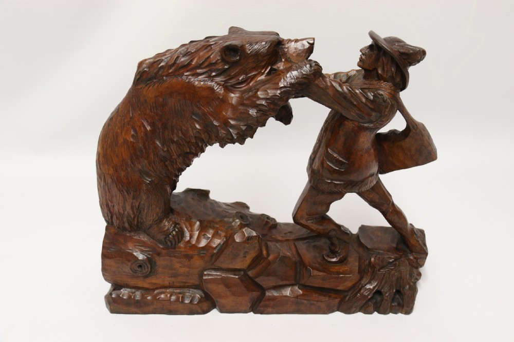 A late 19th-century carved wooden figure group depicting a huntsman battling a rearing bear on a log-form base. View XVII