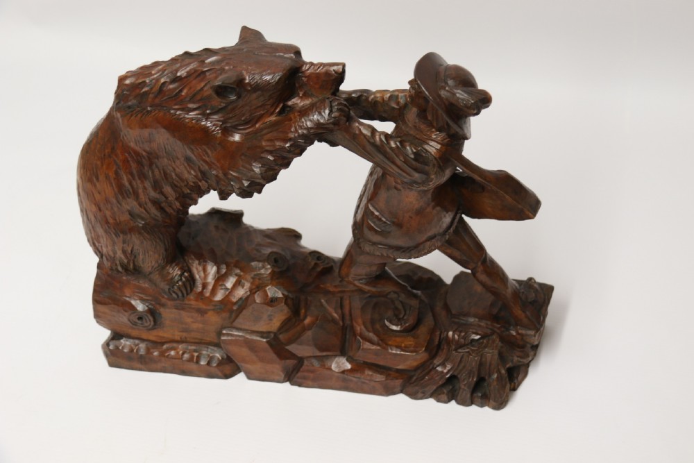 A late 19th-century carved wooden figure group depicting a huntsman battling a rearing bear on a log-form base. View XIX