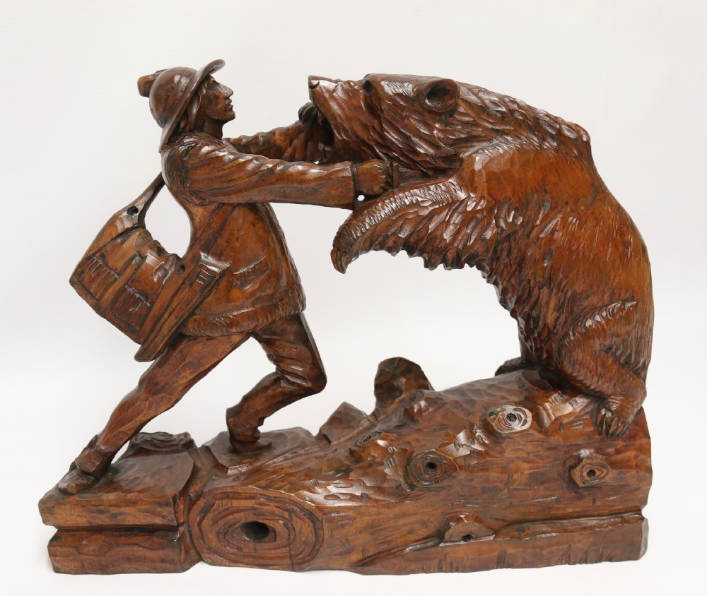 A late 19th-century carved wooden figure group depicting a huntsman battling a rearing bear on a log-form base.