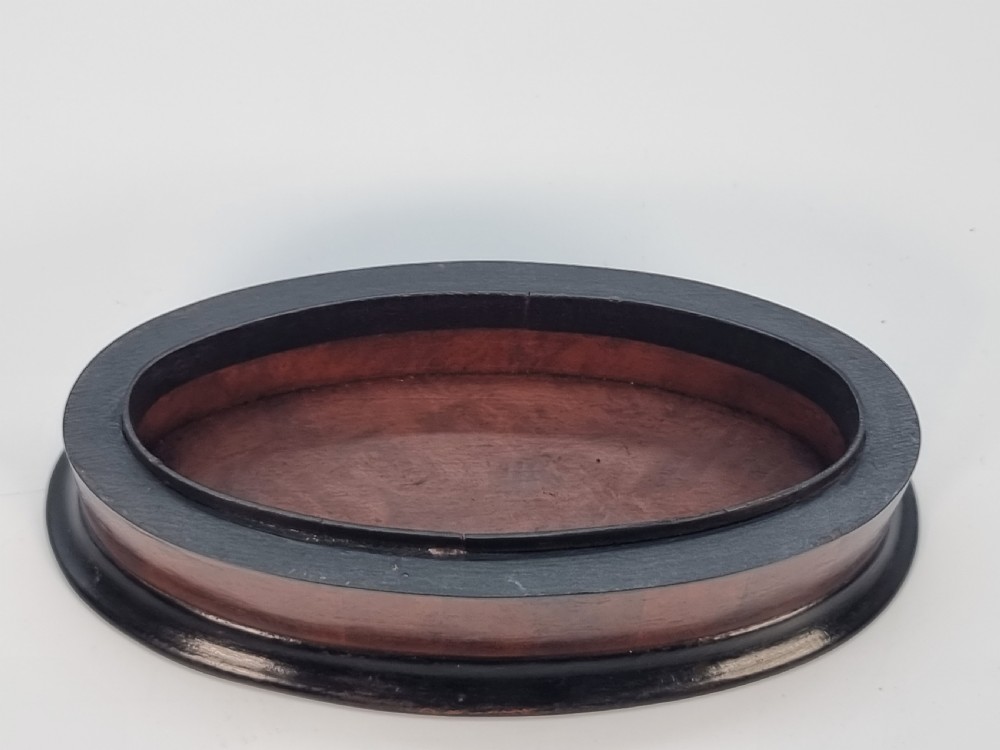An oval wooden box constructed with radially segmented burr walnut veneer, a dark central oval inlay, and a moulded ebonised base. View II