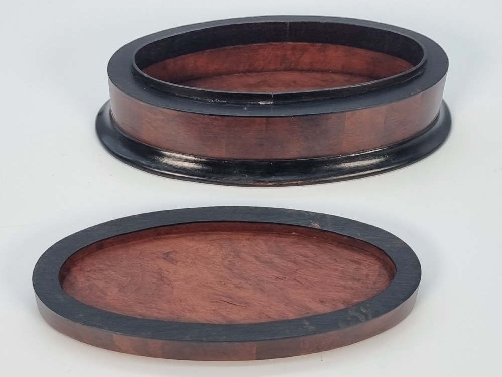 An oval wooden box constructed with radially segmented burr walnut veneer, a dark central oval inlay, and a moulded ebonised base. View V