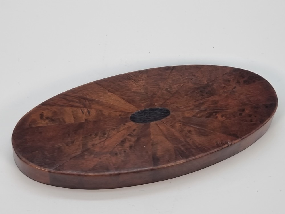 An oval wooden box constructed with radially segmented burr walnut veneer, a dark central oval inlay, and a moulded ebonised base. View VII