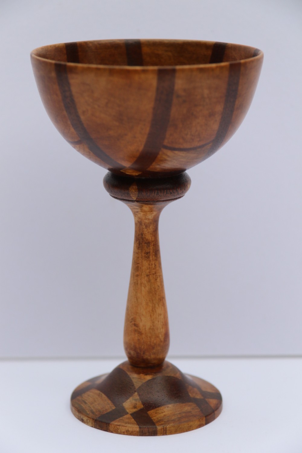 A turned wooden goblet crafted from contrasting specimen woods with a flared rim, a slender stem, and a round patterned base.