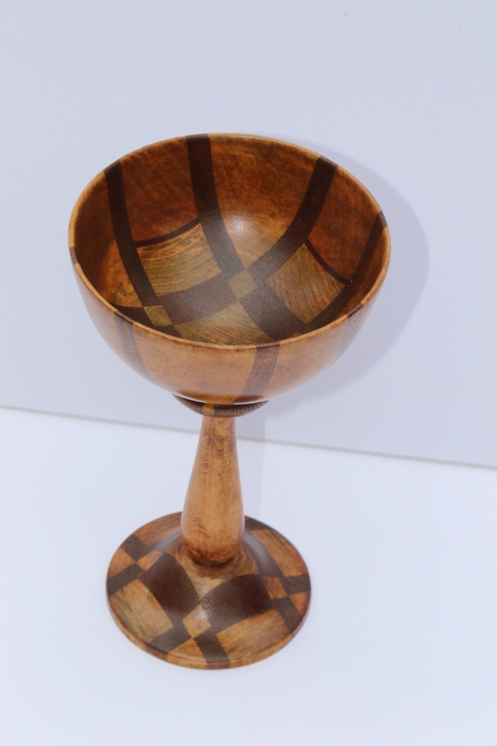 A turned wooden goblet crafted from contrasting specimen woods with a flared rim, a slender stem, and a round patterned base. View II