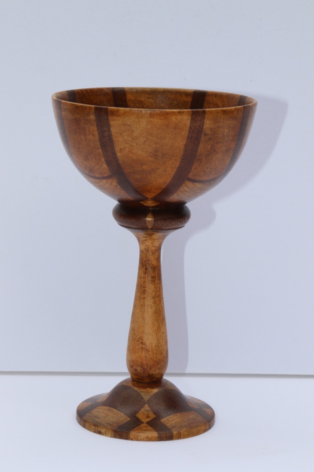 A turned wooden goblet crafted from contrasting specimen woods with a flared rim, a slender stem, and a round patterned base. View X
