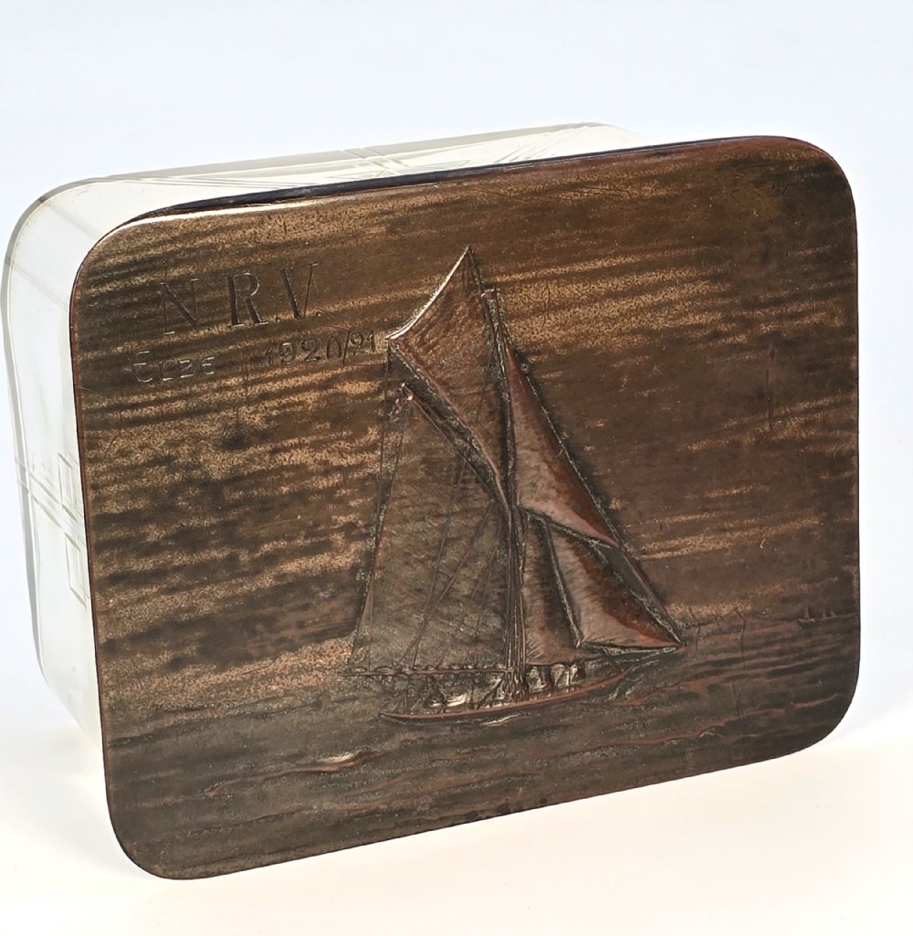 A clear glass rectangular box with a patinated bronze lid featuring a raised relief depiction of a sailing boat.