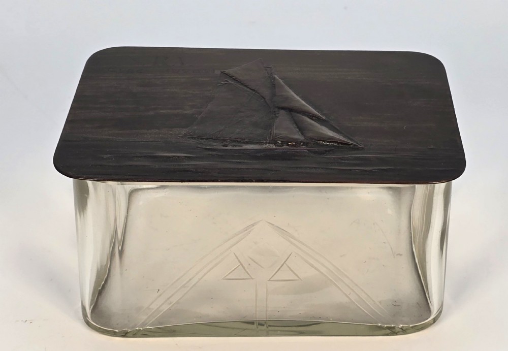 A clear glass rectangular box with a patinated bronze lid featuring a raised relief depiction of a sailing boat. View IX