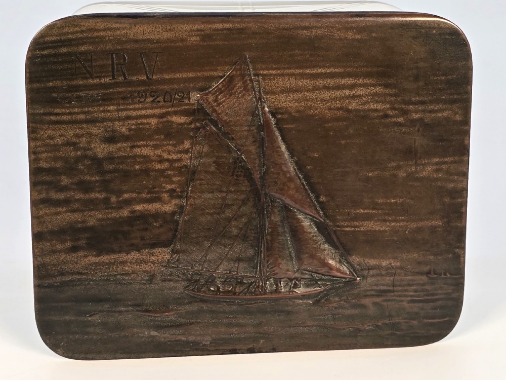 A clear glass rectangular box with a patinated bronze lid featuring a raised relief depiction of a sailing boat. View X