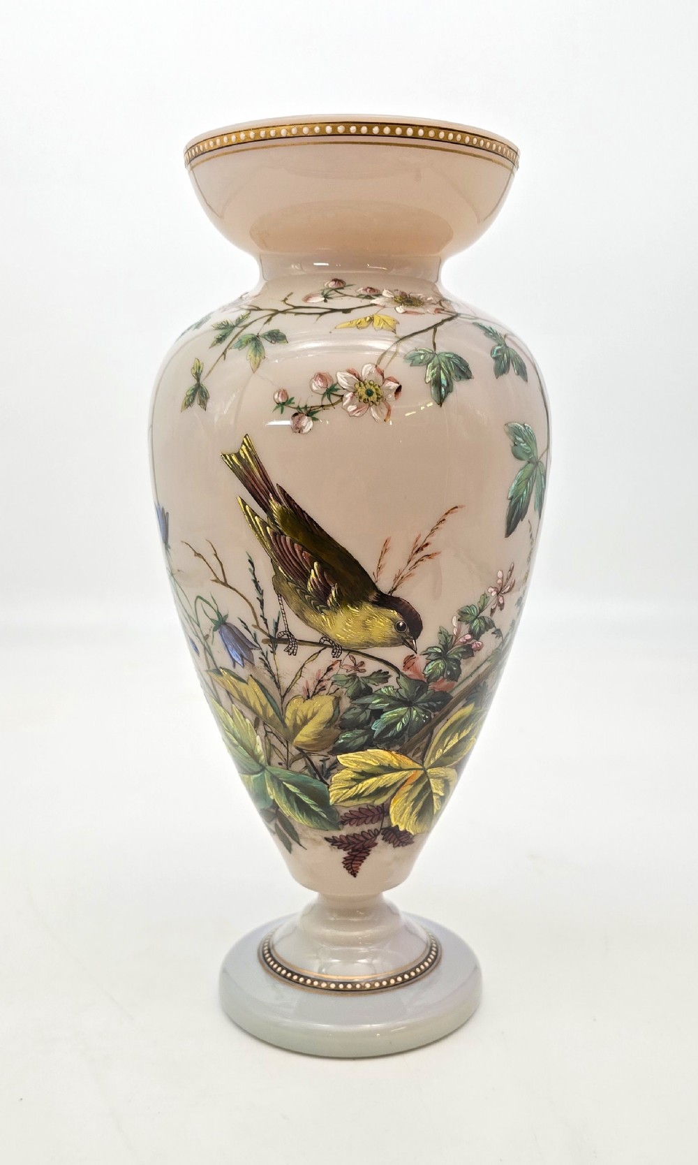 A Victorian opalescent blush pink glass urn vase decorated with hand-painted enamel illustrations of a songbird, delicate blossoms, and gilt trim along the flared rim and base.