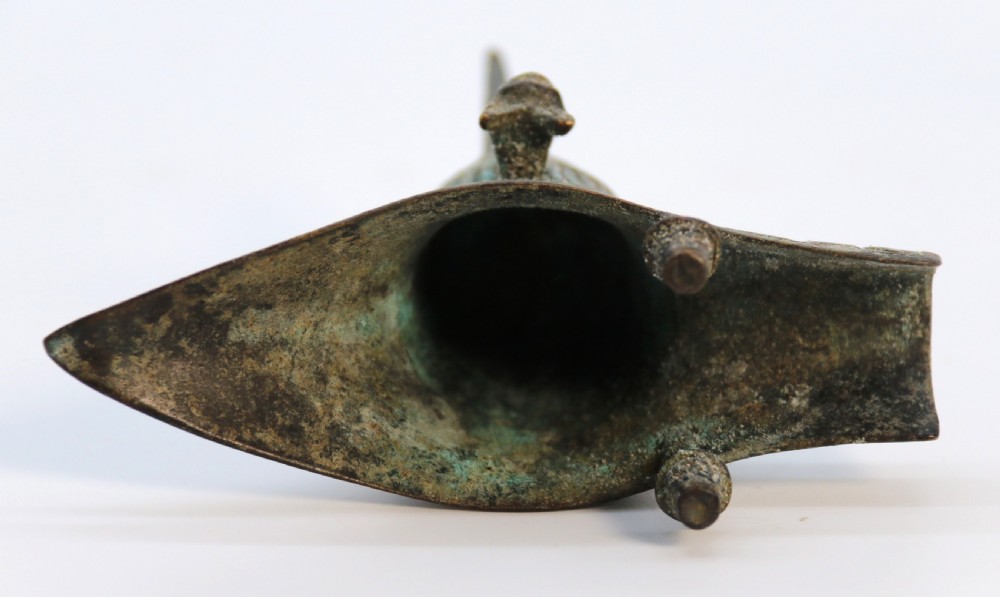 An archaic Chinese patinated bronze tripod wine vessel featuring flared splayed legs, a extended pouring spout with two capped upright posts, and carved relief geometric bands. View XII