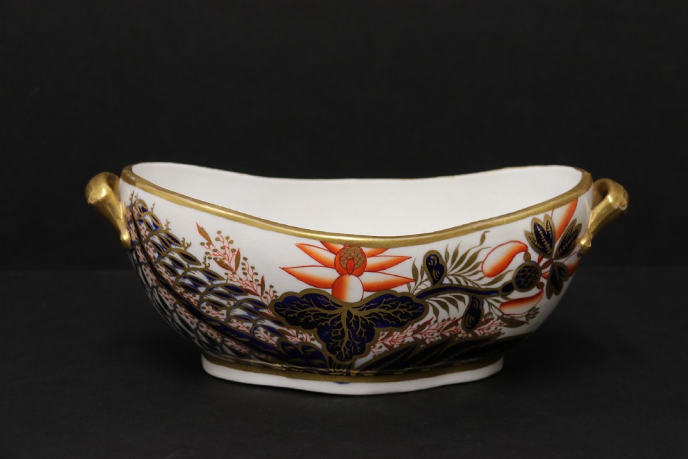 An early nineteenth-century boat-shaped white porcelain shallow dish with gilded side handles, decorated in hand-painted Imari floral motifs in cobalt blue, iron red, and gold.