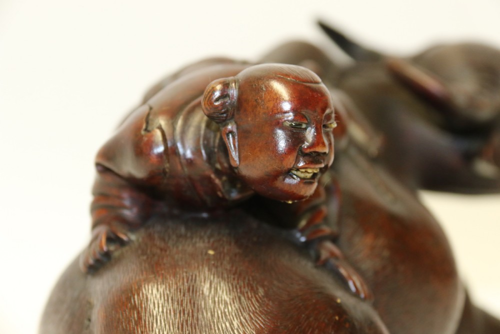 A pair of late Qing dynasty hand-carved dark hardwood water buffaloes, each mounted on a pierced wooden base and depicting a small boy resting on its back. View VII