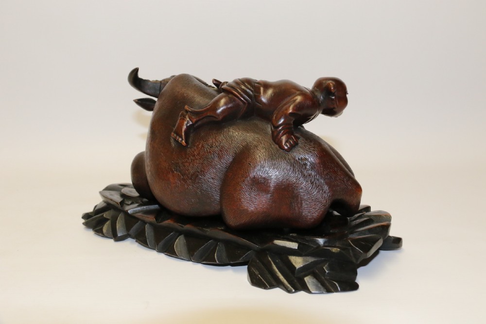 A pair of late Qing dynasty hand-carved dark hardwood water buffaloes, each mounted on a pierced wooden base and depicting a small boy resting on its back. View VIII