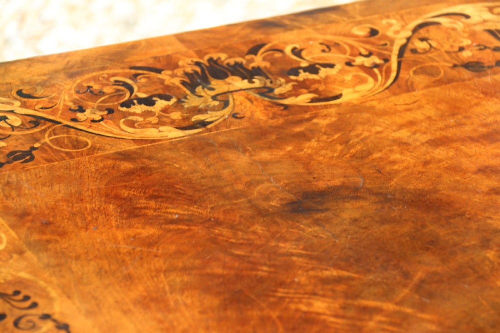 An early 19th-century flame mahogany library table featuring floral marquetry top borders, two frieze drawers with brass knobs, and carved trestle legs connected by a turned stretcher. View VI