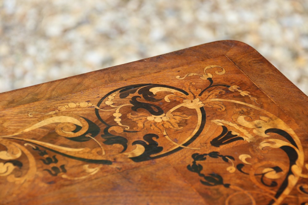 An early 19th-century flame mahogany library table featuring floral marquetry top borders, two frieze drawers with brass knobs, and carved trestle legs connected by a turned stretcher. View VII