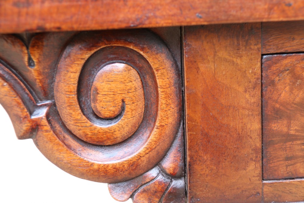 An early 19th-century flame mahogany library table featuring floral marquetry top borders, two frieze drawers with brass knobs, and carved trestle legs connected by a turned stretcher. View VIII