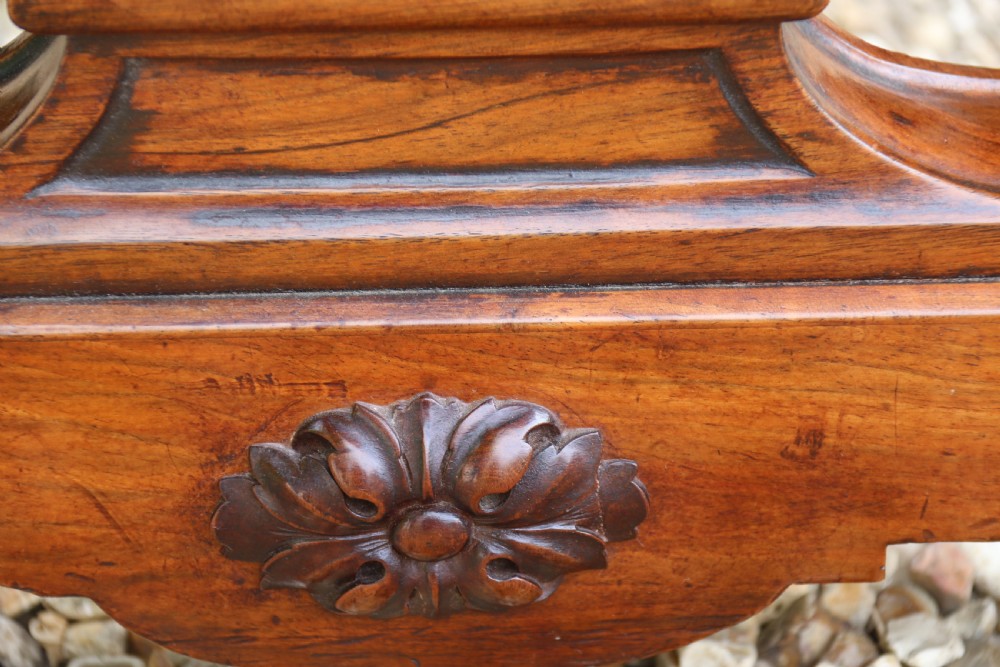 An early 19th-century flame mahogany library table featuring floral marquetry top borders, two frieze drawers with brass knobs, and carved trestle legs connected by a turned stretcher. View IX