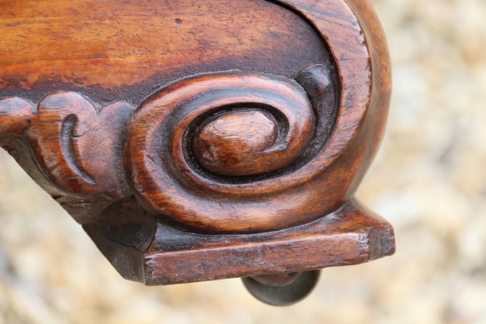 An early 19th-century flame mahogany library table featuring floral marquetry top borders, two frieze drawers with brass knobs, and carved trestle legs connected by a turned stretcher. View XV