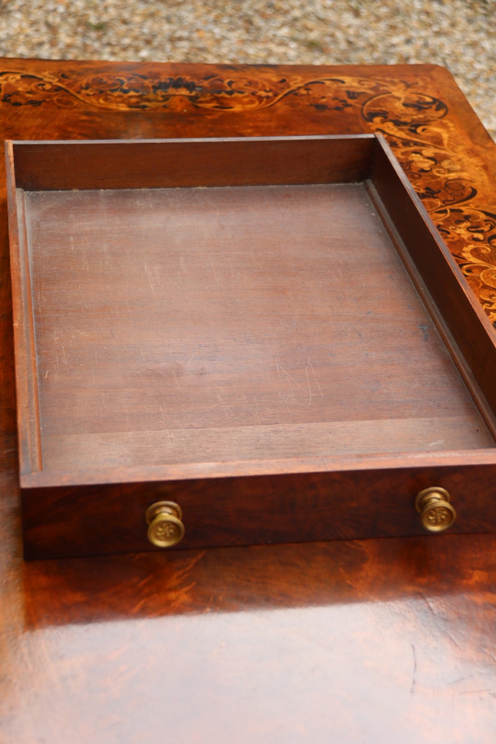An early 19th-century flame mahogany library table featuring floral marquetry top borders, two frieze drawers with brass knobs, and carved trestle legs connected by a turned stretcher. View XXII