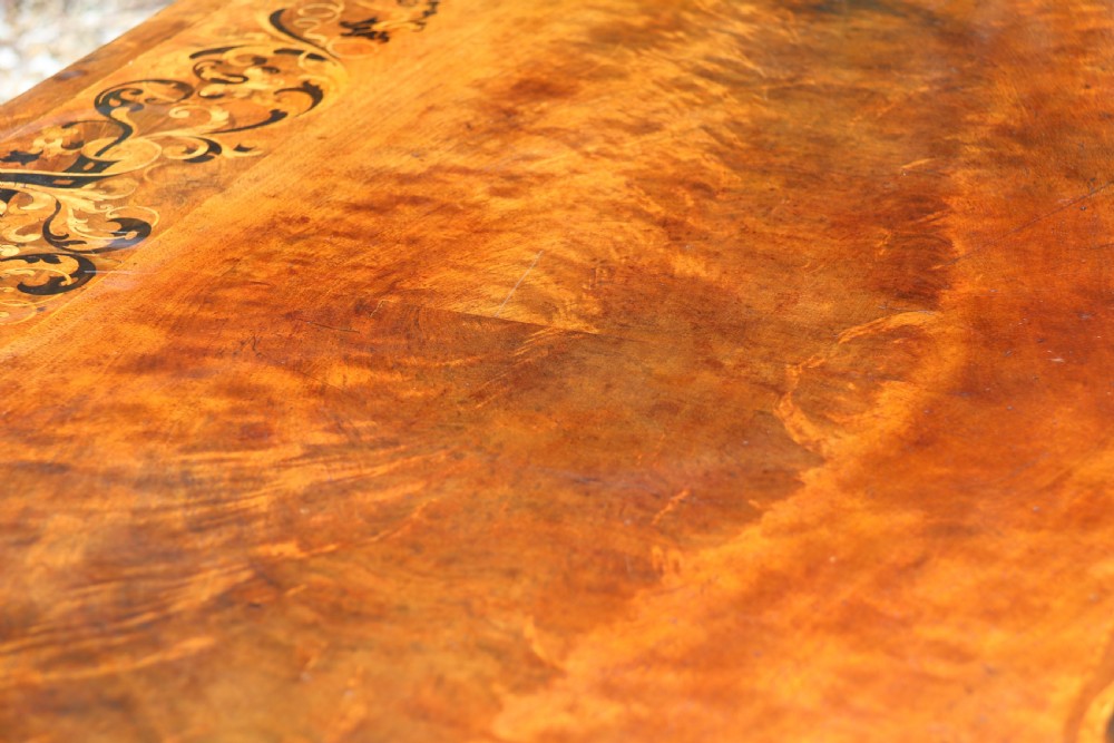 An early 19th-century flame mahogany library table featuring floral marquetry top borders, two frieze drawers with brass knobs, and carved trestle legs connected by a turned stretcher. View XXVII
